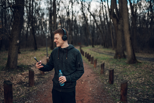 Redhead runner athlete taking a break from his workout and using smartphone while training in the forest. Healthy lifestyle concept.