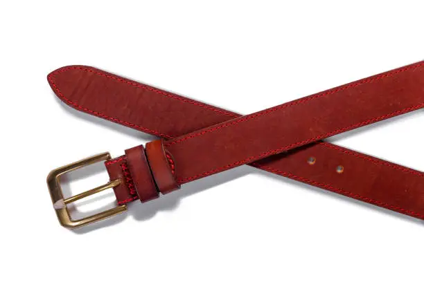 Photo of A crossed brown leather belt with a metal buckle on a white background is isolated.