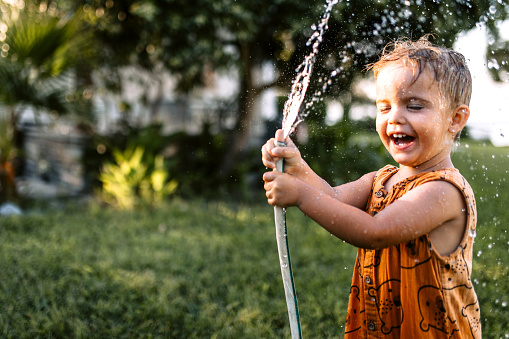 Little boy playing with garden hose in backyard, having fun with spraying water.