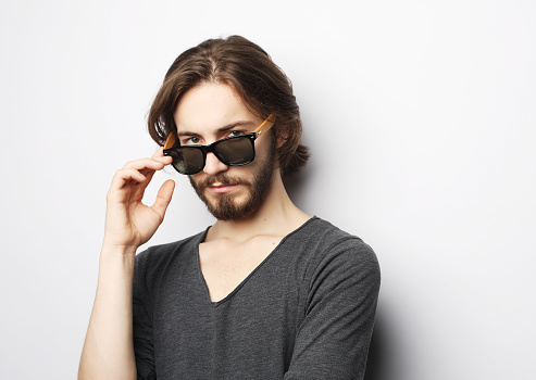 Portrait of a fashionable young bearded man in sunglasses over white background