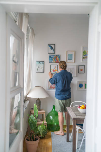 istock Young man organizes photos on wall in dining room 1425694443