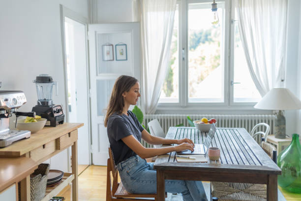 istock Young woman works on laptop at dining room table 1425694697