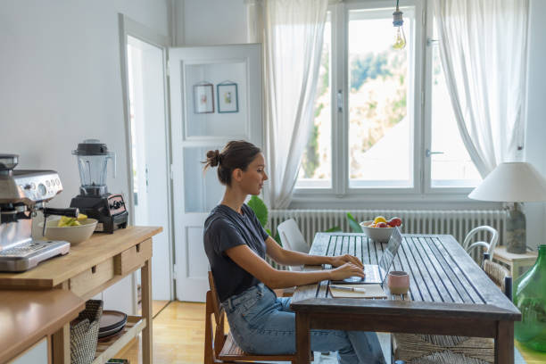 istock Young woman works on laptop at dining room table 1425694710