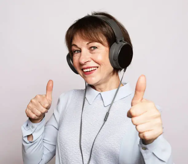 Lifestyle, tehnology and people concept: Elderlywoman listening music and showing thumbs up over white background