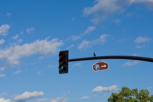 Parking sign and traffic light against a blue sky background with puffy cumulus clouds. Concept image of this way towards parking with a green light and copy space.