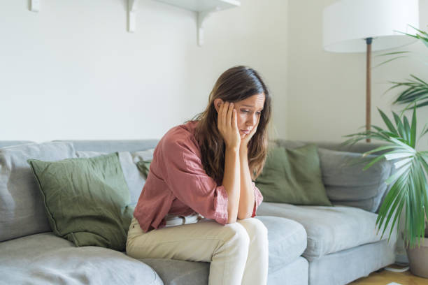 Sad young woman  on sofa in living room stock photo