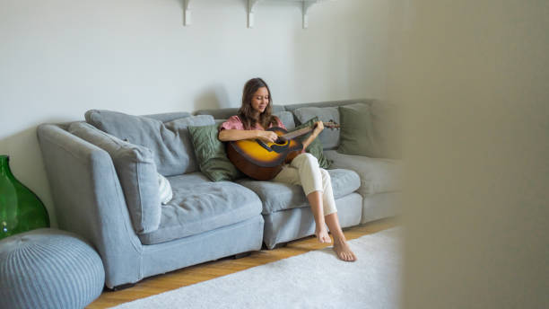 istock Young woman plays guitar on sofa 1425698419