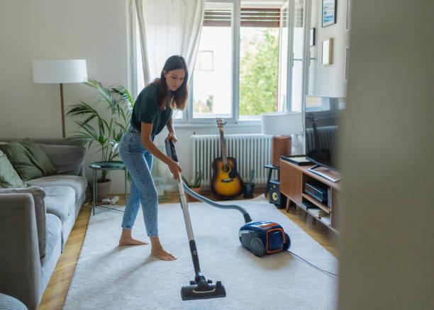 Young woman vacuums living room carpet stock photo