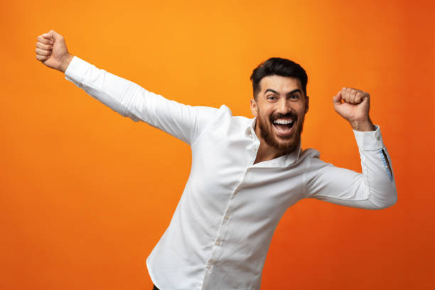istock Young man celebrating and dancing against orange background in studio 1425720000