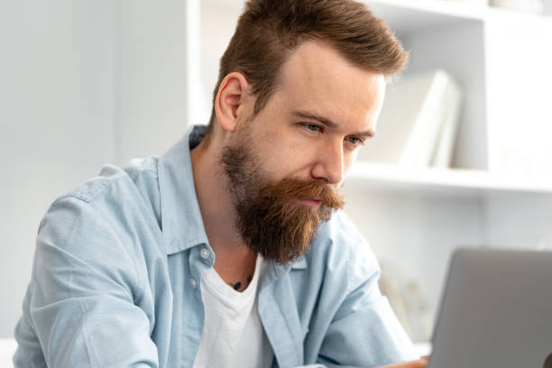 istock Thoughtful tired young bearded man sitting at the table working on laptop 1425720016