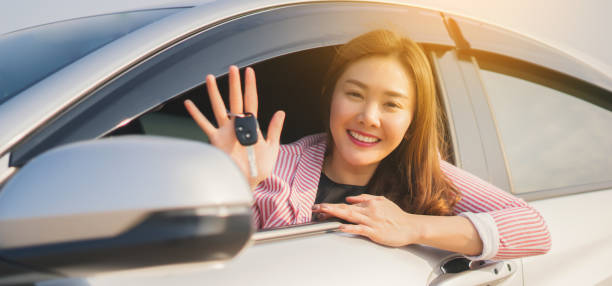 Asian driver woman smiling and showing new car key while sitting in a car that she taking it from dealer in the auto show. transport business, car sale for consumerism and people concept,vintage color stock photo