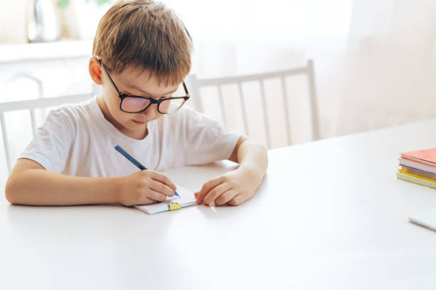 istock A boy in eyeglasses writes letters in a notebook with a pen 1425727751
