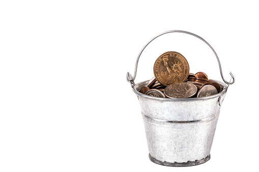 Miniature metal bucket filled with American coins on a white background