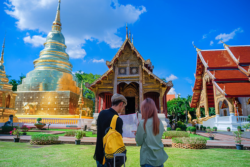 Young tourists looking at map before a beautiful golden temple in Chiang Mai. They check up the right famous place to visit.