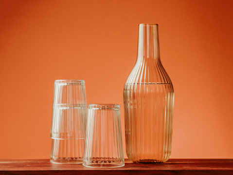 Water carafe and drinking glasses in studio orange background still life