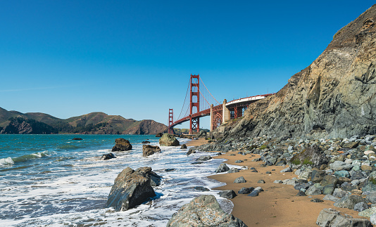 Image of Stunning sandy beach waves crashing into rocks covered in mussels by Golden Gate Bridge on foggy morning