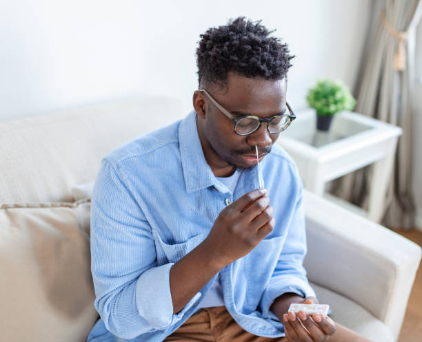 istock African-American man using cotton swab while doing coronavirus PCR test at home. man using coronavirus rapid diagnostic test. Young man at home using a nasal swab for COVID-19. 1425771735