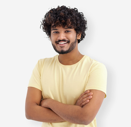 Portrait of happy Asian man guy with curly hair and white teeth in a yellow t-shirt standing on a white background looking at camera and smiles friendly