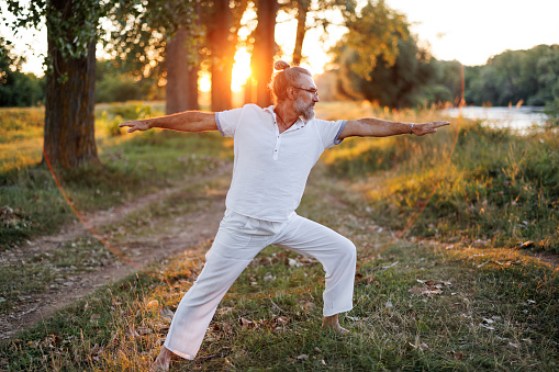 One mature man practicing warrior yoga pose in nature at sunset