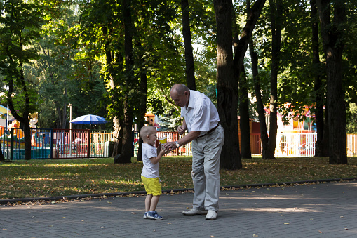 Grandfather and grandson are walking in the park along the path with a glass of popcorn. An old man and a little boy have snacks on the go...