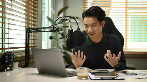 istock Young podcaster using a microphone and laptop computer recording audio for channel in home studio. 1425784262