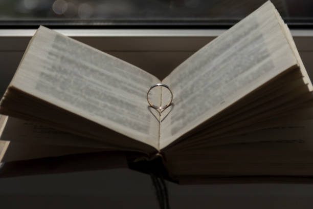 istock Wedding ring with a falling shadow in the form of a heart standing on an open book. 1425790366