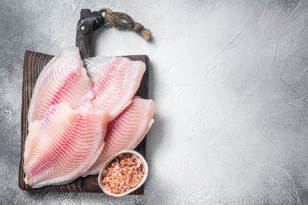 istock Uncooked tilapia fish fillet on a wooden board. White background. Top view. Copy space 1425791169