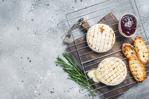 Grilled Camembert cheese on grill with cranberry sauce and toast. Gray background. Top view. Copy space.