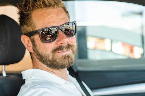 Close up portrait of handsome young man wearing sunglasses in the car.