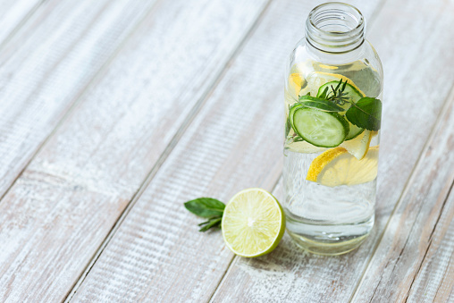 Infused water jar on white wood with lemon and cucumber slices.