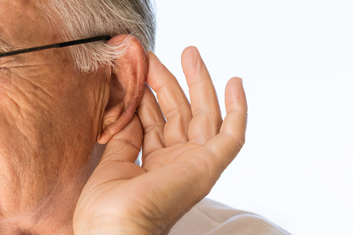 Senior man is touching his ear to hear better in front of white background.