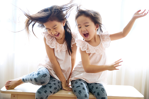 2 cute little lovely asian sisters sitting at home laughing and playing together