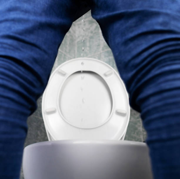 Prostatitis concept. Rear view of a man, hard to pee. Difficulty urinating with prostatitis. View of the toilet and the legs of a man. Imitation of urine with clear water. Sick in the toilet stock photo