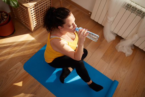 Woman training inside the living room, exercising at home, pause and drinking water.