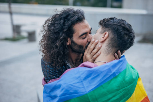 istock Gay couple wrapped in rainbow flag hugging 1425812176