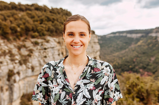 Close-up portrait of cheerful woman wears floral hawaiian shirt, enjoys on top of rocky mountain. Adventure, travel, holiday concept.