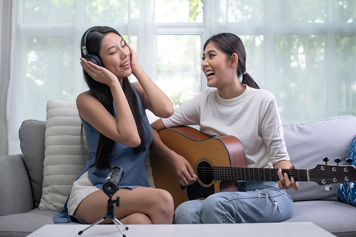 Young Asian lesbian couples play music and sing together having fun at home. LGBT couple lifestyle concept.