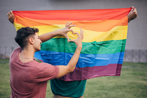 Gay man holding a heart symbol with his hands on rainbow flag