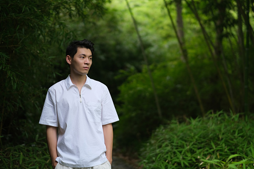 Handsome Asian young man at green bamboo grove, looking away