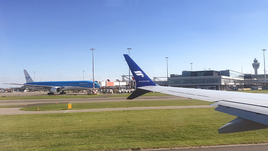 Iceland Air Plane Wing  with KLM Boeing in background, Schipol Airport, Amsterdam, Netherlands - 22 June 2022 : The Iceland Air plane wing can be seen against the backdrop of a KLM Boeing plane ready for take off at Schipol Airport, the main International airport in The Netherlands