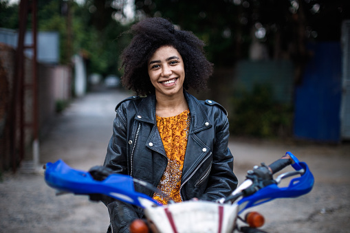 Beautiful girl with afro hair, wearing biker jacket, riding a dirt bike, smiling  in Tay Ho, Hanoi, Vietnam