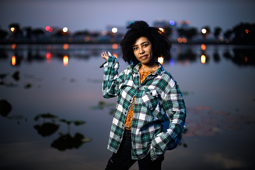 Beautiful girl with afro hair, wearing a plaid oversized shirt, having fun at the lakeside in the dusk at Tay Ho, Hanoi, Vietnam