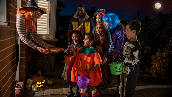 Two families wearing fancy dress, out trick or treating in North East England during halloween. They are standing at their neighbour's front door, getting ready to collect sweets.
