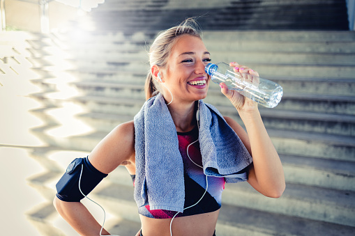 Cropped shot of a young woman enjoying a bottle of water while workingout during the day. Sporty young woman drinking water while exercising outdoors