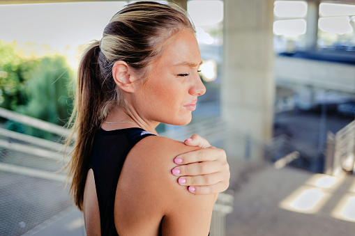 Closeup shot of a sporty young woman holding her shoulder in pain while exercising outdoors.
