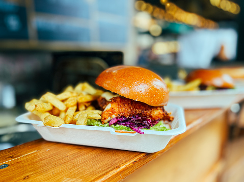 Close up image of a freshly flame grilled shredded chicken burger and fries on a wooden counter at Borough Market, one of the oldest and most famous food markets in the world. The burger and fries are displayed in a white recyclable container. Horizontal colour image with copy space.