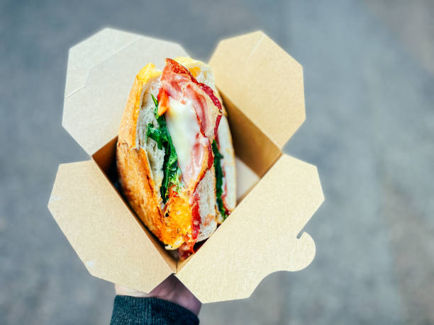 istock Man holding toasted bacon and cheese sandwich in recyclable cardboard container 1425846671
