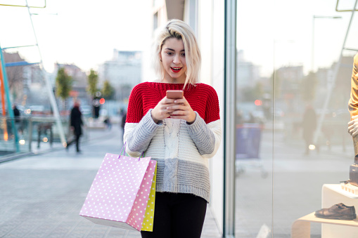 Front view of a young woman standing in a shopping center while using a mobile phone