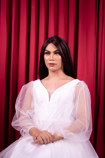 Glamour woman with a white wedding dress sitting in front of the red curtain inside the studio