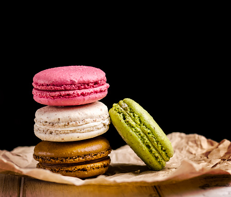 Retro pastel colorful macaroon cookies on black background with copyspace. Homemade french macaron dessert with different flavors: chocolate, strawberry, vanilla, pistachio. Candy shop sweet menu design.